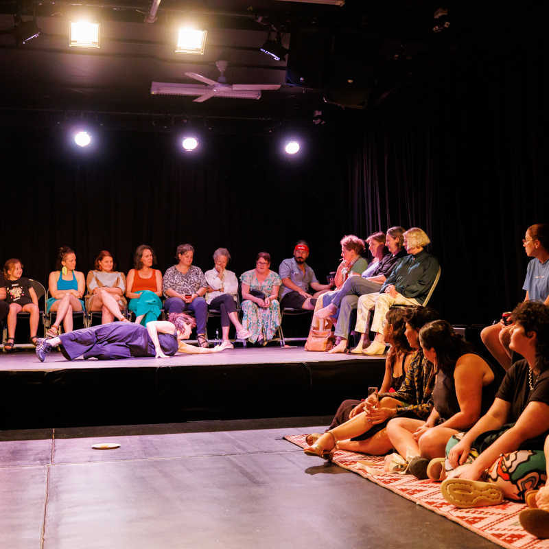 Photograph of people sitting around a room watching a performer