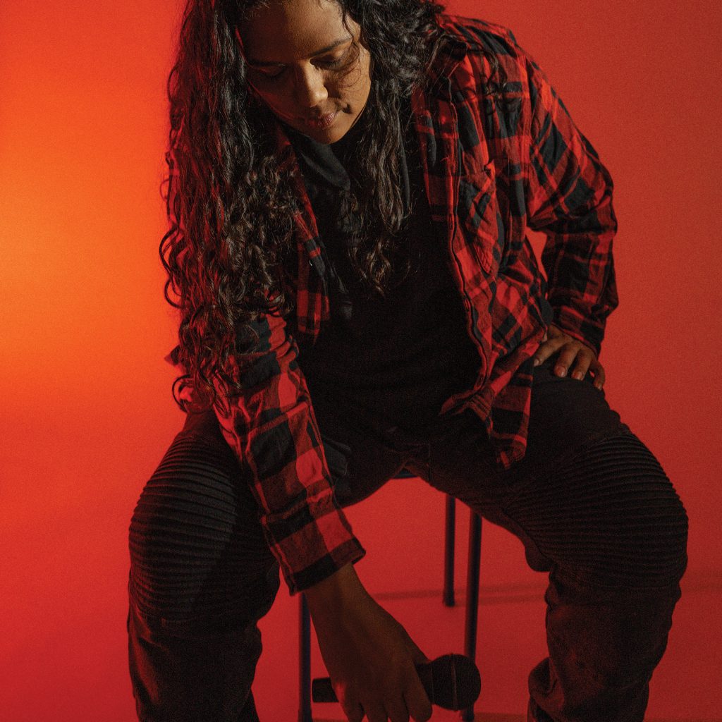 Photograph of artist Melanie sitting on a chair and looking down at the ground holding a microphone