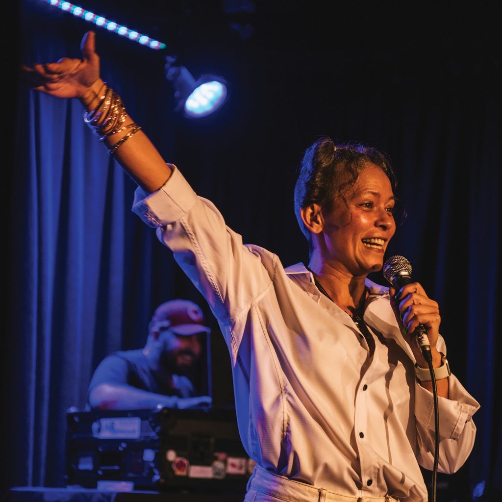 Photograph of artist Natalie with her hand in the air holding a microphone