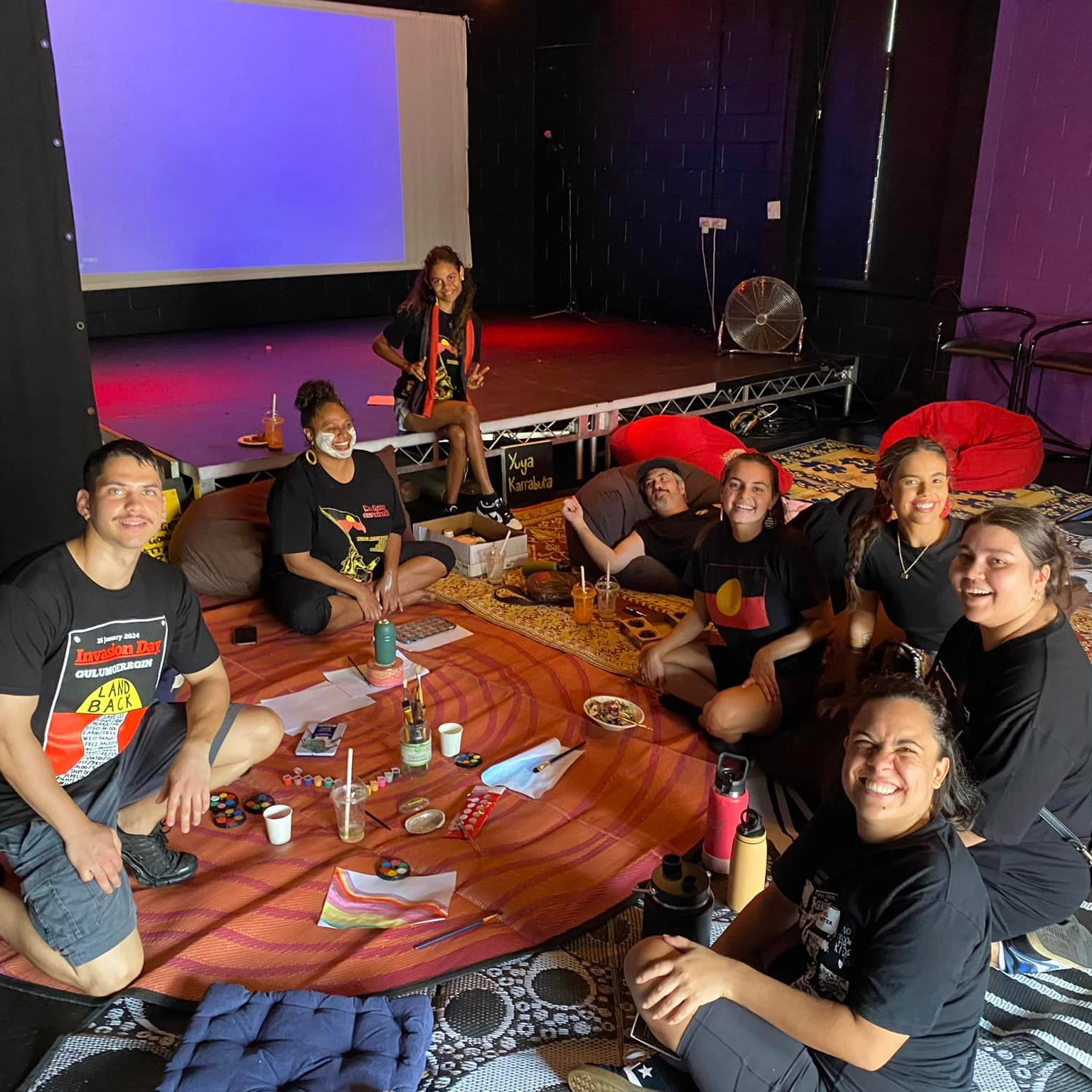 Photograph of a group of people sitting in a circle smiling at the camera.