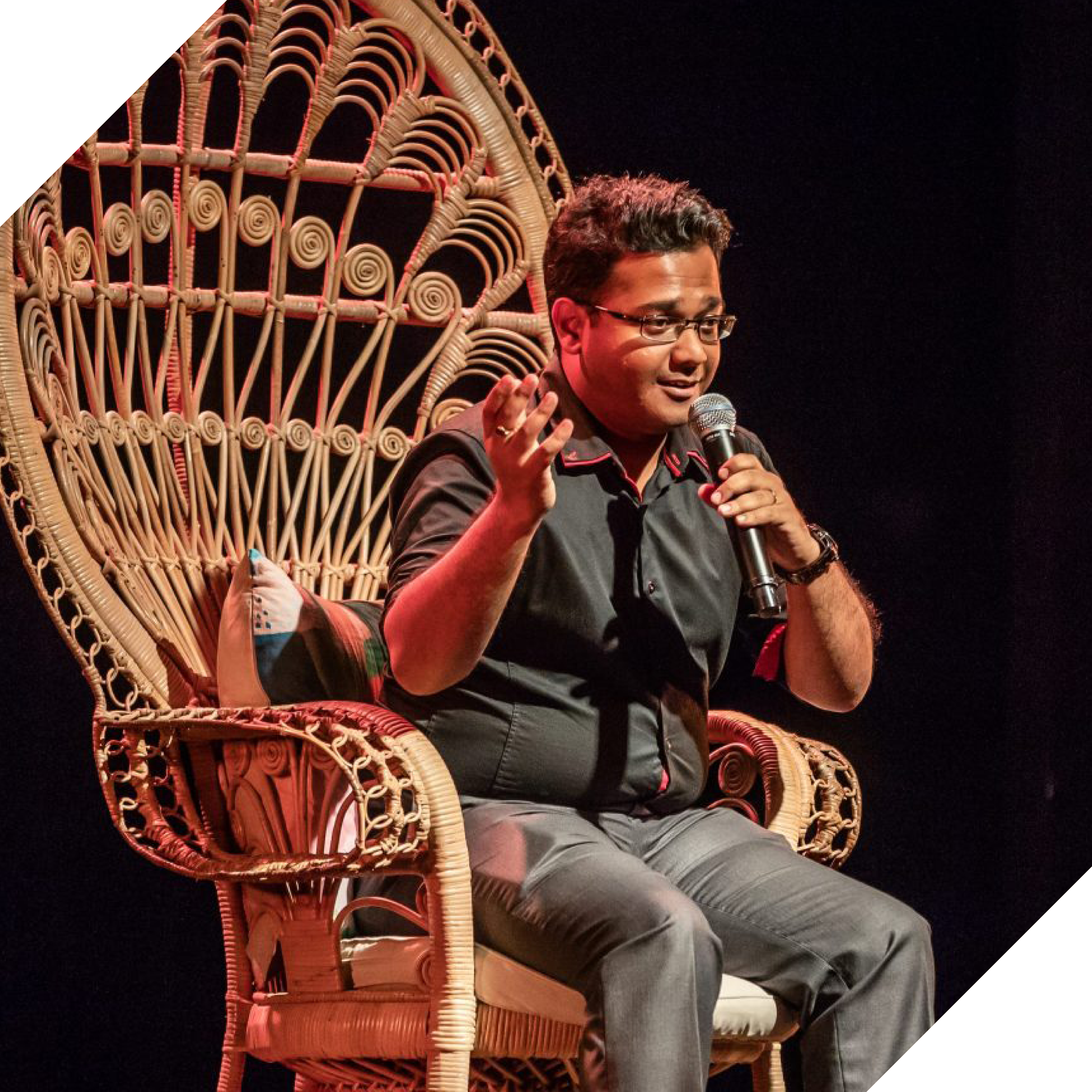 Photograph of someone sitting in a huge woven chair holding a mic