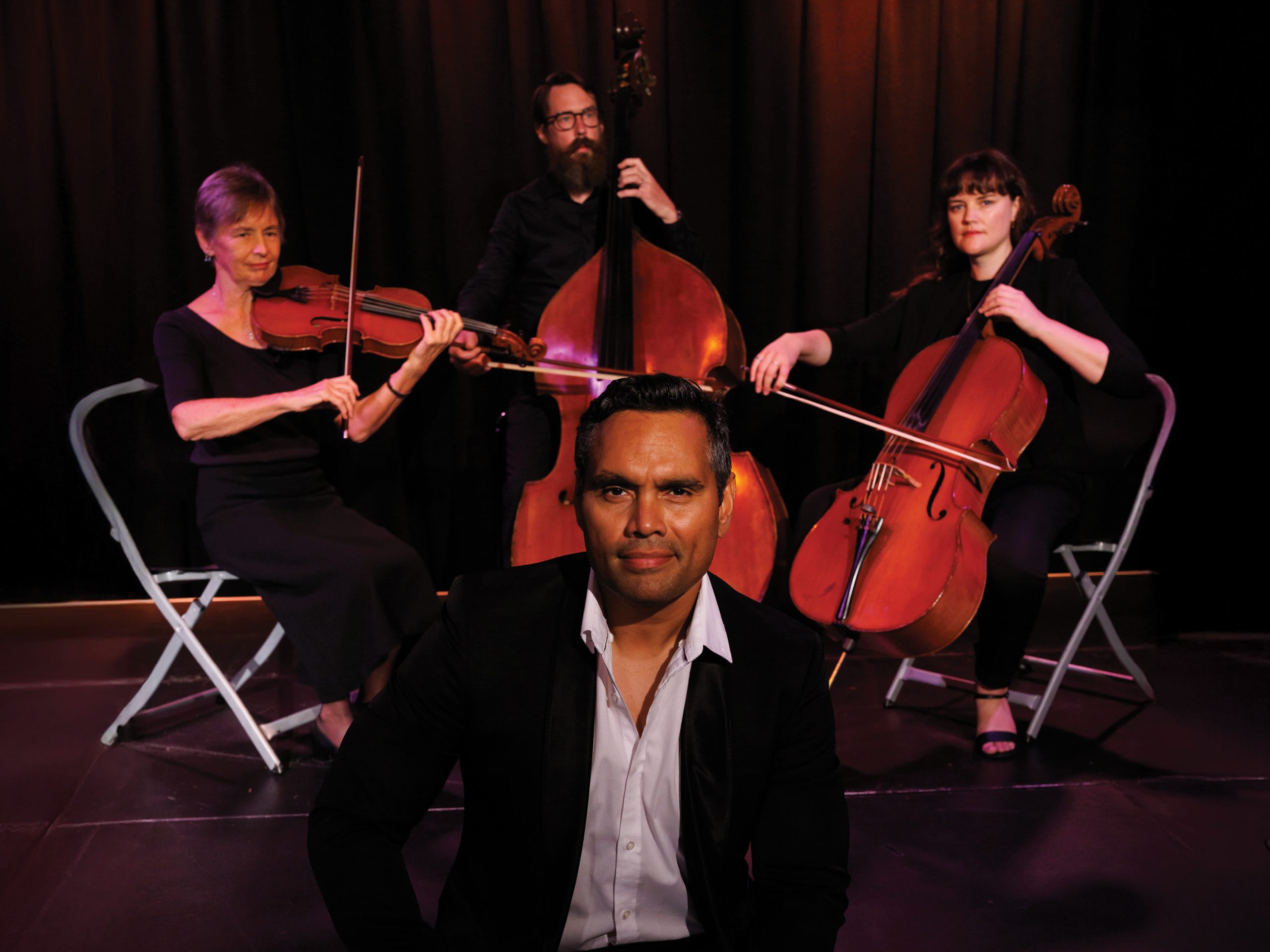 Photo of actor Rob Collins sitting in front of 3 musicians
