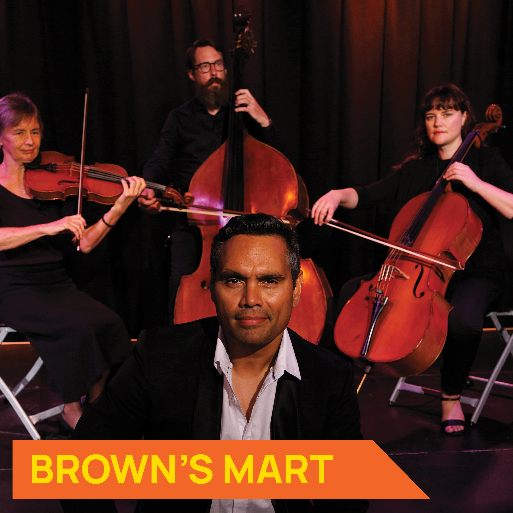 Photo of actor Rob Collins sitting in front of 3 musicians